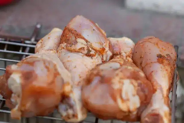 Raw seasoned chicken drumsticks on a grill