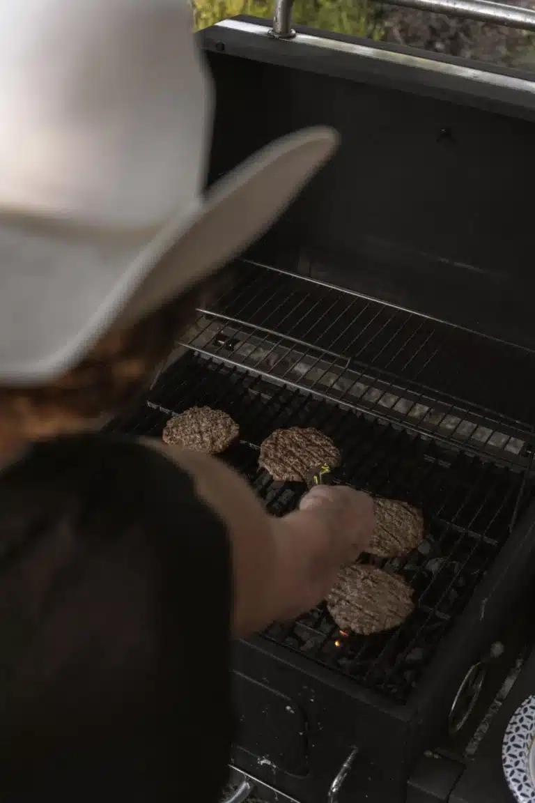 Person in cowboy hat grilling burgers on an outdoor BBQ