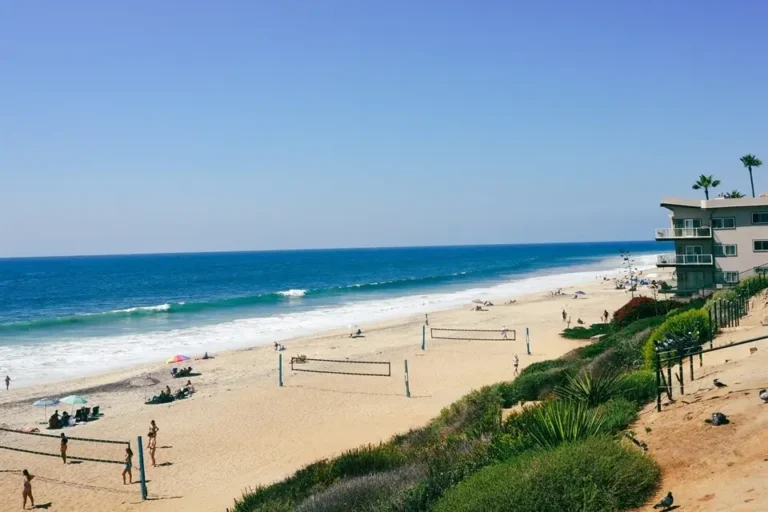 Carlsbad State Beach on a sunny day, with beach volleyball courts, clear ocean water.