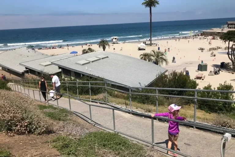 A view of Moonlight Beach in Encinitas, CA, with families enjoying the sand and ocean on a clear day.