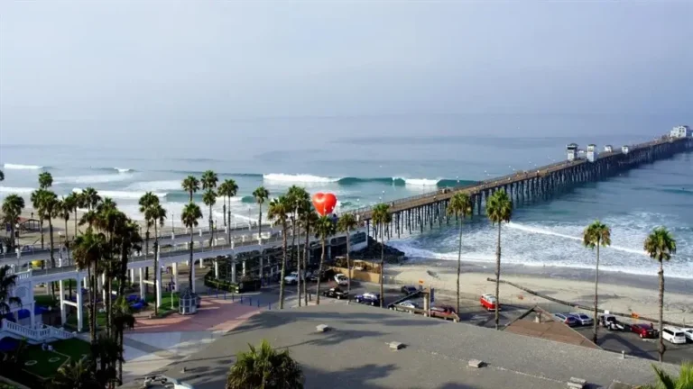 Aerial view of Oceanside pier extending into the Pacific Ocean, with surrounding beach and palm trees.