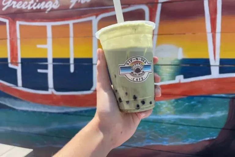 A refreshing drink from Sip-N-Sea Cafe held up against a vibrant mural backdrop in Encinitas, CA.