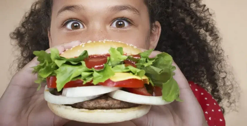 Child biting into a large gourmet hamburger