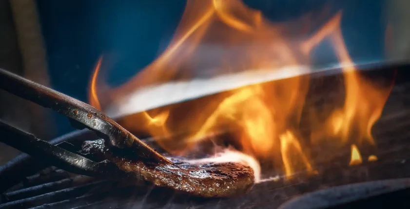 Spatula flipping a steak with flames on grill