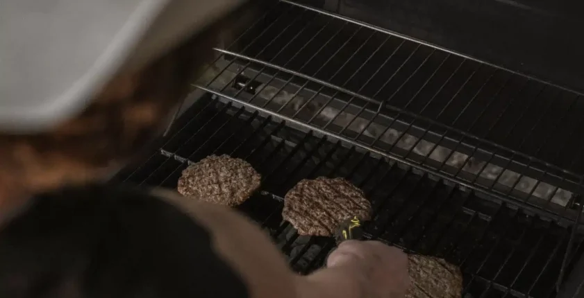 Person in cowboy hat grilling burgers on an outdoor BBQ